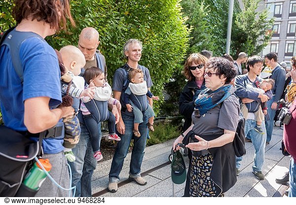 A tourist speaks with members of the NYC Dads Group celebrating International Babywearing Week with their stroll on the High Line  wearing their babies. City Dads Groups celebrated the day in thirteen cities taking their own walks in iconic landmark locations. The babies and their nurturing dads attracted much attention from the other visitors showing off the benefits of carrying their children in this manner. The baby carrier company Britax contributed carriers to many of the members as a show of support.