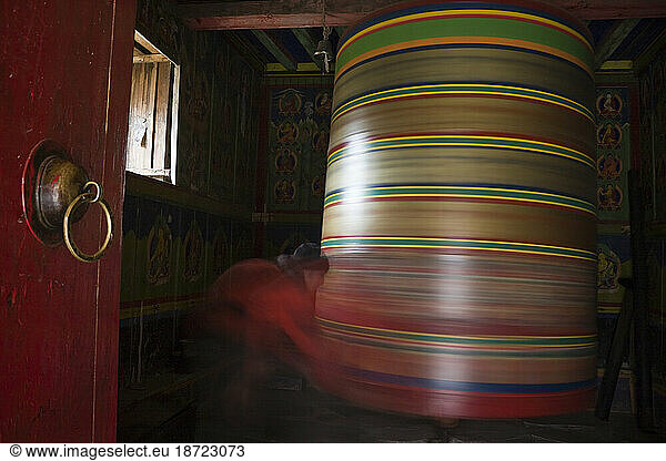 A trekker spins a giant prayer wheel at the Buddhist nunnery in Devuche  Khumbu region  Himalaya Mountains  Nepal.