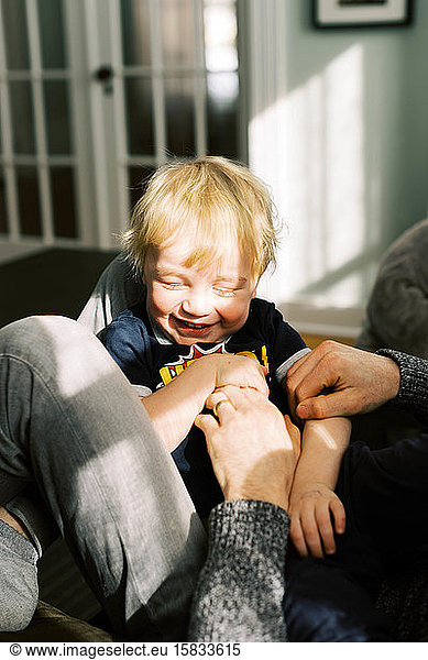 A two year old boy laughing with his eeditorial closed while being tickled.