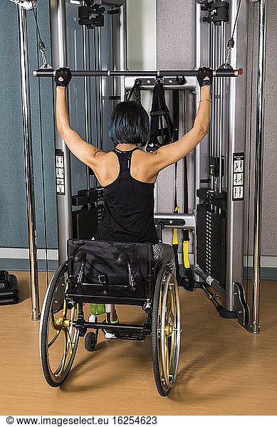 A view from behind of a paraplegic woman working out using a lat pull down machine in a fitness facility; Sherwood Park  Alberta  Canada