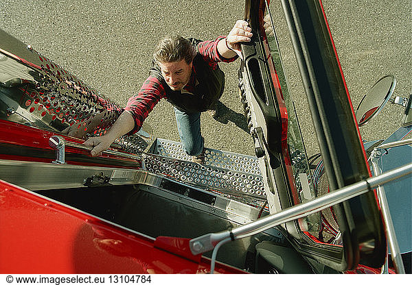 A view looking down of a truck driver climbing into the cab of a commercial truck .