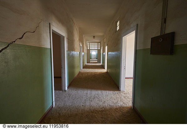 A view of a corridor in a derelict building full of sand. Vivid green coloured walls. Shadows