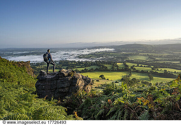 A walker stood on a rock at Cloudside looking across the Cheshire Plains  Congleton  Cheshire  England  United Kingdom  Europe