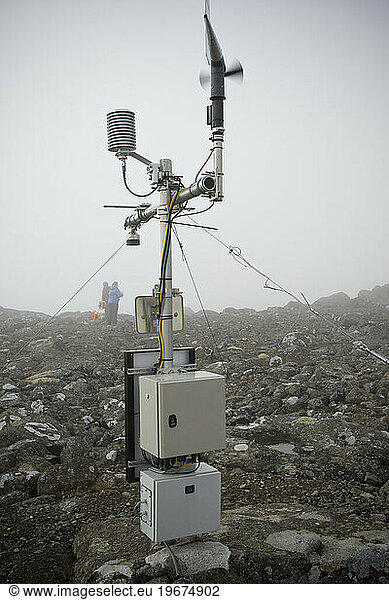 A weather station sits in the clouds while two figures work on scientific measurements for climate change studies.
