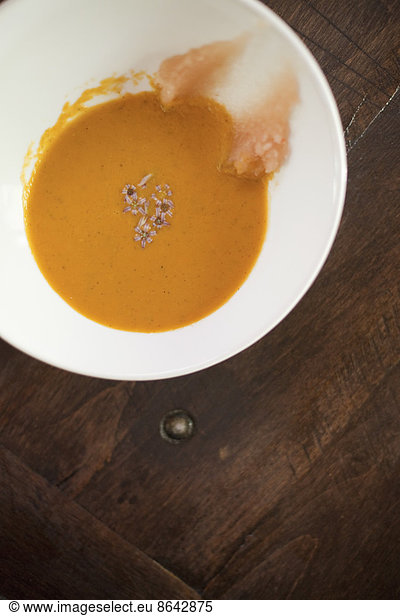 A white china bowl with a creamy soup and garnish  viewed from above. A rouille puree on the side of the dish.
