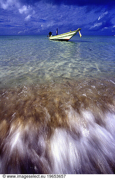 A wide angle view of a long tail boat  with waves crashing on the beach in the foreground  Koh Phangan.