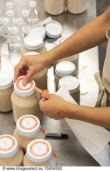 A woman affixes labels on glass jars containing pecan milk