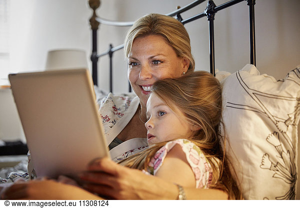 A woman and a child sitting in bed watching a laptop screen.