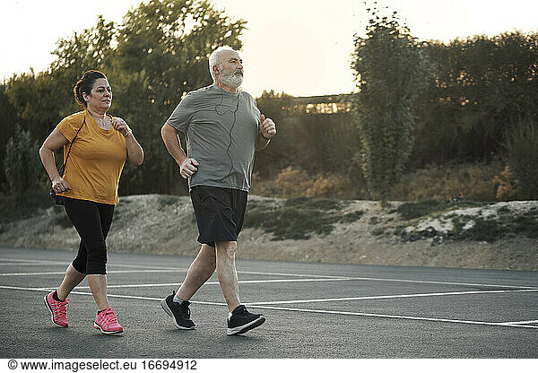 A woman and an elderly man are jogging in the street