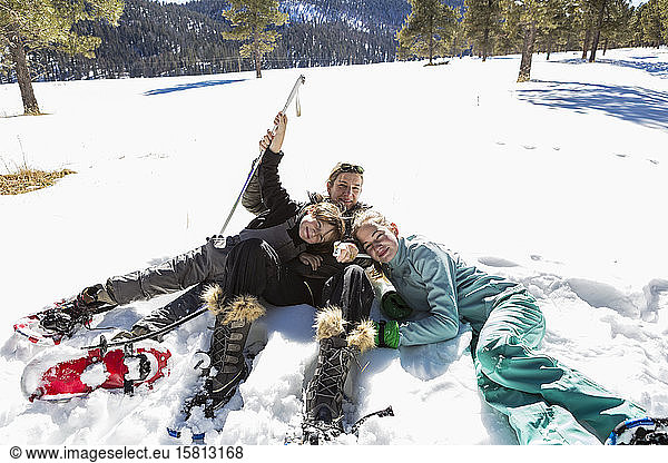 A woman and her two children  teenage girl and a young boy lying in the snow in snow shoes and ski gear.