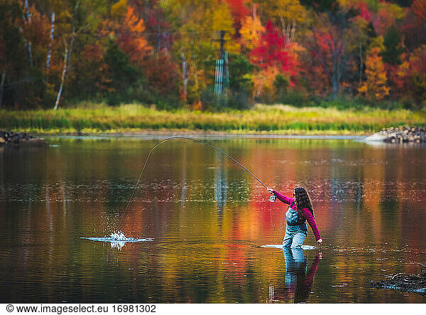 A woman angler catches a fish during fall foliage season