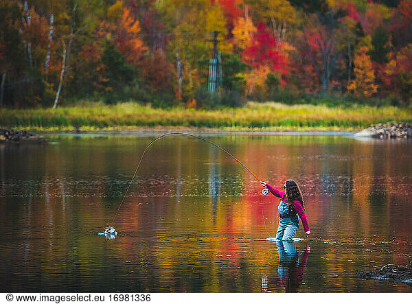 A woman angler catches a fish during fall foliage season