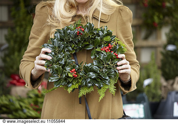 A woman carrying a decorated wreath of holly and evergreen leaves.