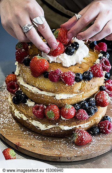 A woman cook assembling a layer cake with fresh cream and fresh fruit  strawberries and blueberries.