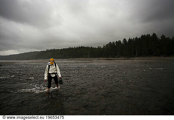 A woman crosses the Ozette River at low tide as dark clouds approach during a hiking trip on the coast of Olympic National Park  Washington.