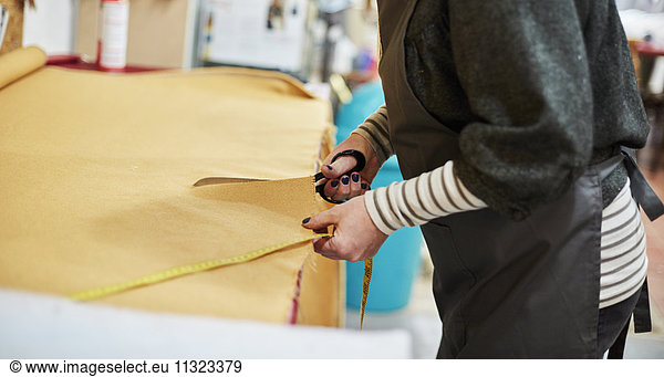 A woman cutting out yellow upholstery fabric on a workbench with a large pair of scissors.