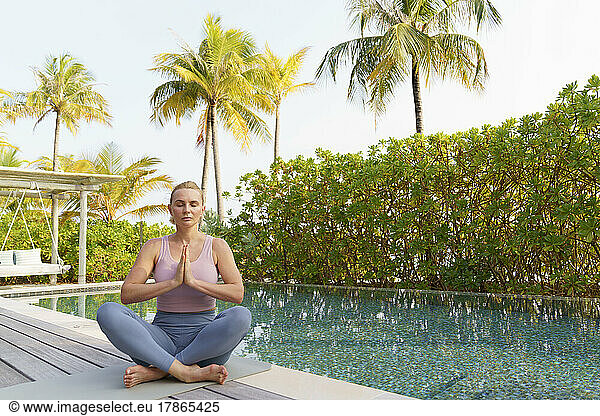 A woman does yoga by the pool  sits in the lotus position.