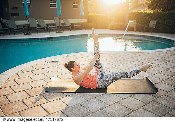 A woman doing mat pilates next to a pool at sunrise in the summer
