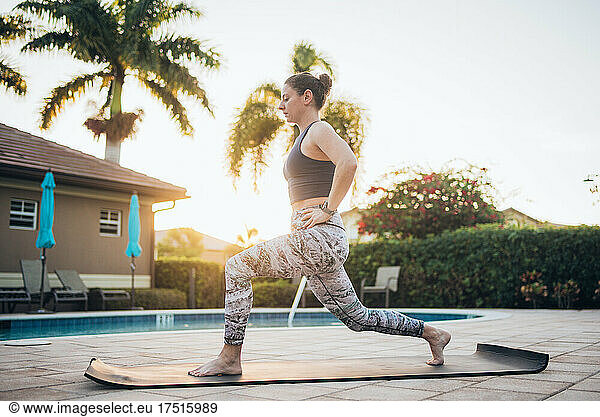 A woman doing mat pilates next to a pool at sunrise in the summer