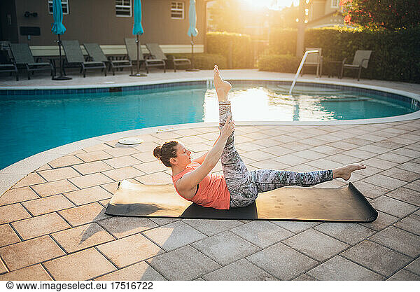 A woman doing mat pilates next to a pool at sunrise in the summer