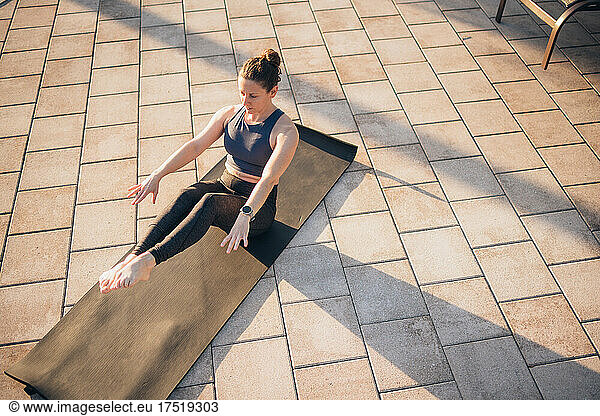 A woman doing mat pilates next to a pool at sunrise in the summer