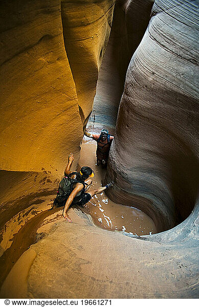 A woman down climbing into pool with man in pool in sculpted slot canyon  Utah.