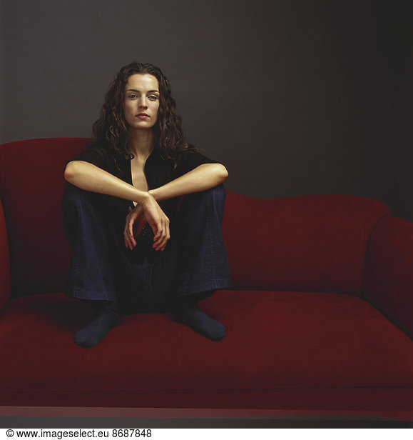 A woman dressed in black seated on a red couch.