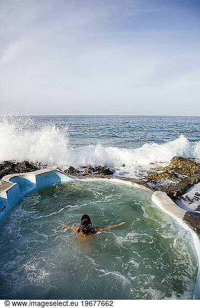 A woman enjoys a small oceanside pool at a local  organic spa resort.