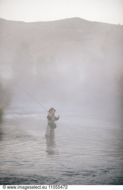 A woman fisherman fly fishing  standing in waders in thigh deep water.