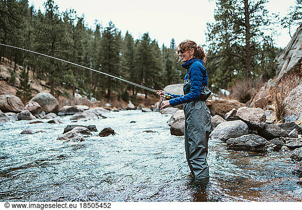A woman fly-fishing in a river with stones and rocks