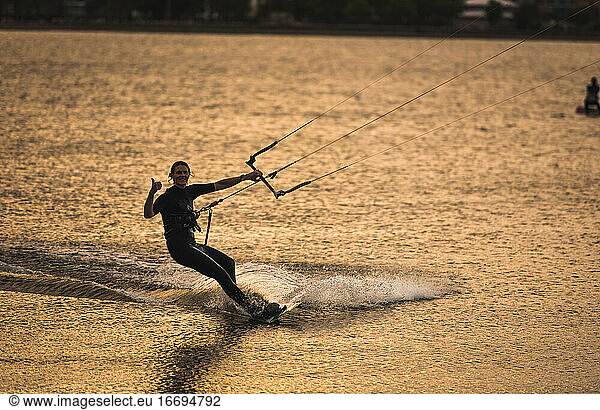 A woman giving up a thumbs up while kiteboarding during late day