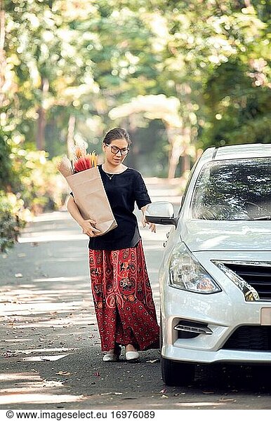 A woman hold a paper bag of dry flower and back to car after shopping
