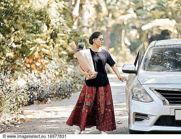 A woman hold a paper bag of dry flower and back to car after shopping