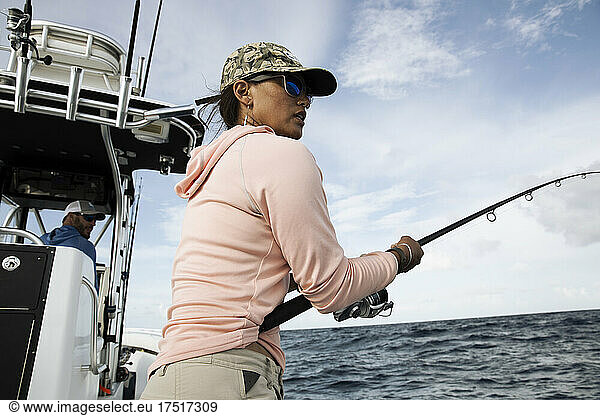 A woman hold fishing rod and looks out to the water on fishing boat