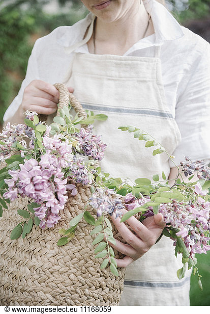 A woman holding a basket of cut branches with pink flowers.
