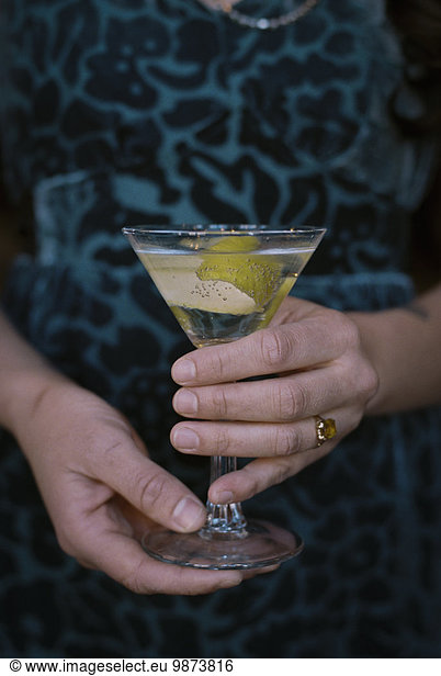 A woman holding a martini glass with a cocktail and a twist of lemon peel.
