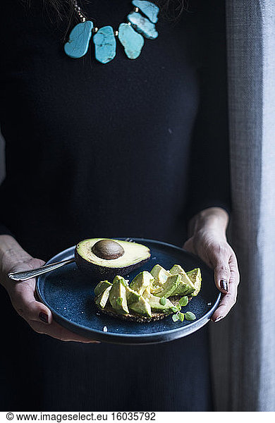 A woman holding a plate of avocado bread