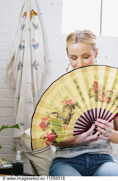 A woman holding an open Oriental fan hiding her face.