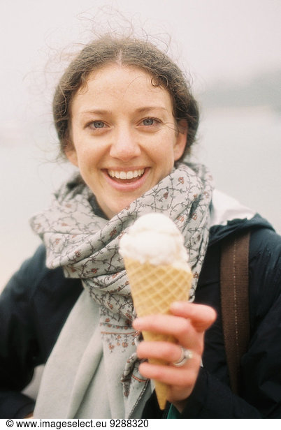 A woman holding out an icecream in a cone and laughing.