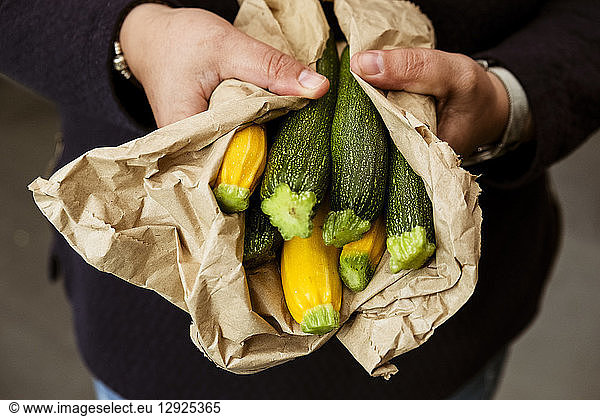 A woman holding out her hands holding a bunch of freshly picked yellow and green courgettes.