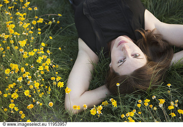 A woman in a black vest top and jeans lying on the grass with her hands behind her head.