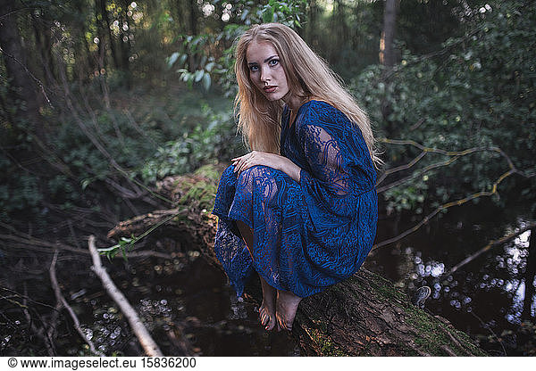 A woman in a blue dress sits on a fallen tree barefoot