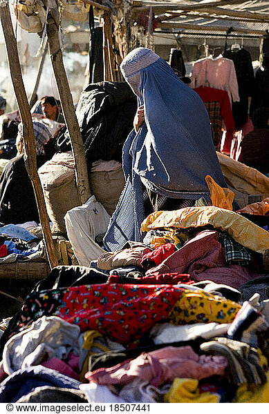 A woman in a burqa makes her way through vendors tables of clothes and textiles at a market in Kabul  Afghanistan.