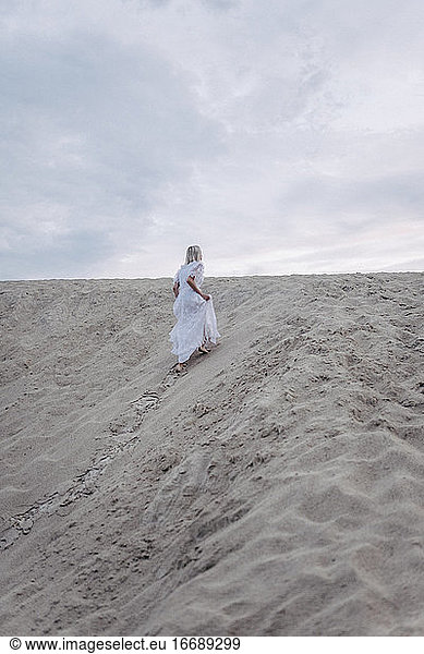 a woman in a dress climbs a sandy hill