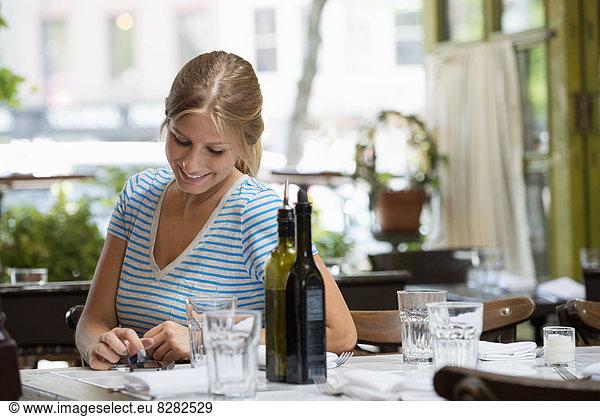 A Woman In A Striped Tee Shirt Sitting At A Table After A Meal  Checking Her Smart Phone.
