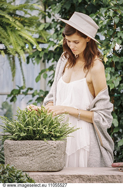 A woman in a sunhat  light clothes and shawl in a garden.