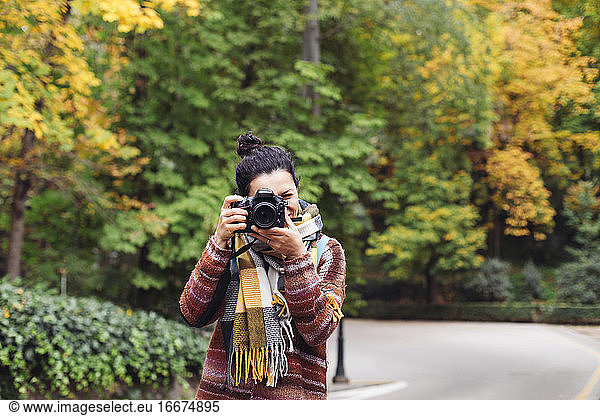A woman in a sweater and scarf taking pictures in an autumn forest