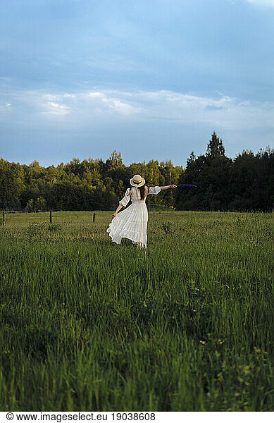 A woman in a white dress and hat runs through a flowering field.