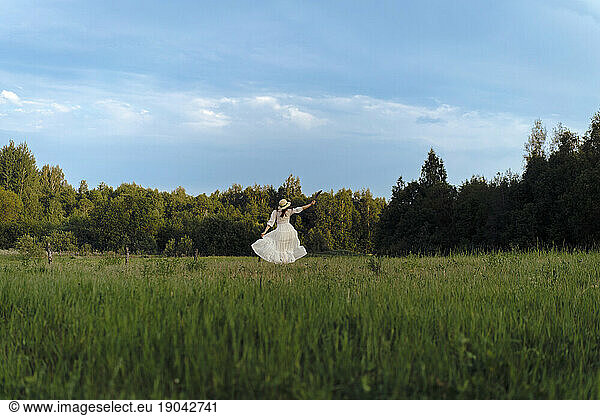 A woman in a white dress and hat runs through a flowering field.