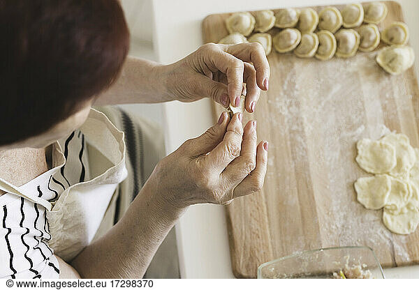 A woman in a white kitchen prepares traditional Russian dumplings from meat and dough